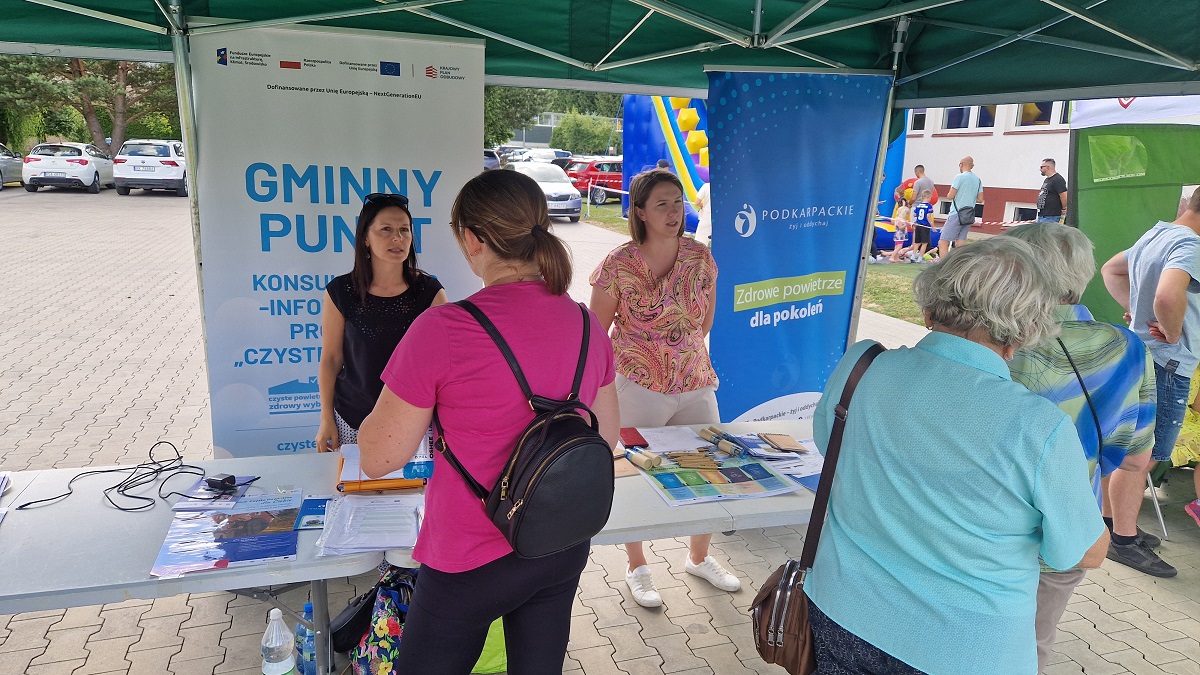 Ludzie przy stoiskach informacyjnych o zdrowiu i środowisku pod namiotem. Bannery z logo i hasłami.